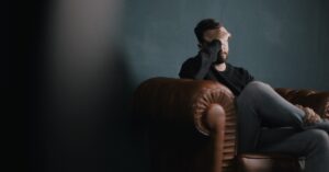 Image of a man with his head in his hands and sitting on a couch.