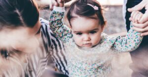 Image of a man and woman helping their daughter walk.