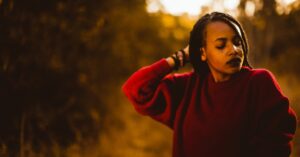 Image of a woman in a red sweater looking down while the sun sets behind her.