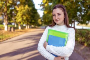 Teenager girl 12-13-14 years old, summer park holds notebooks, folders textbooks in hands